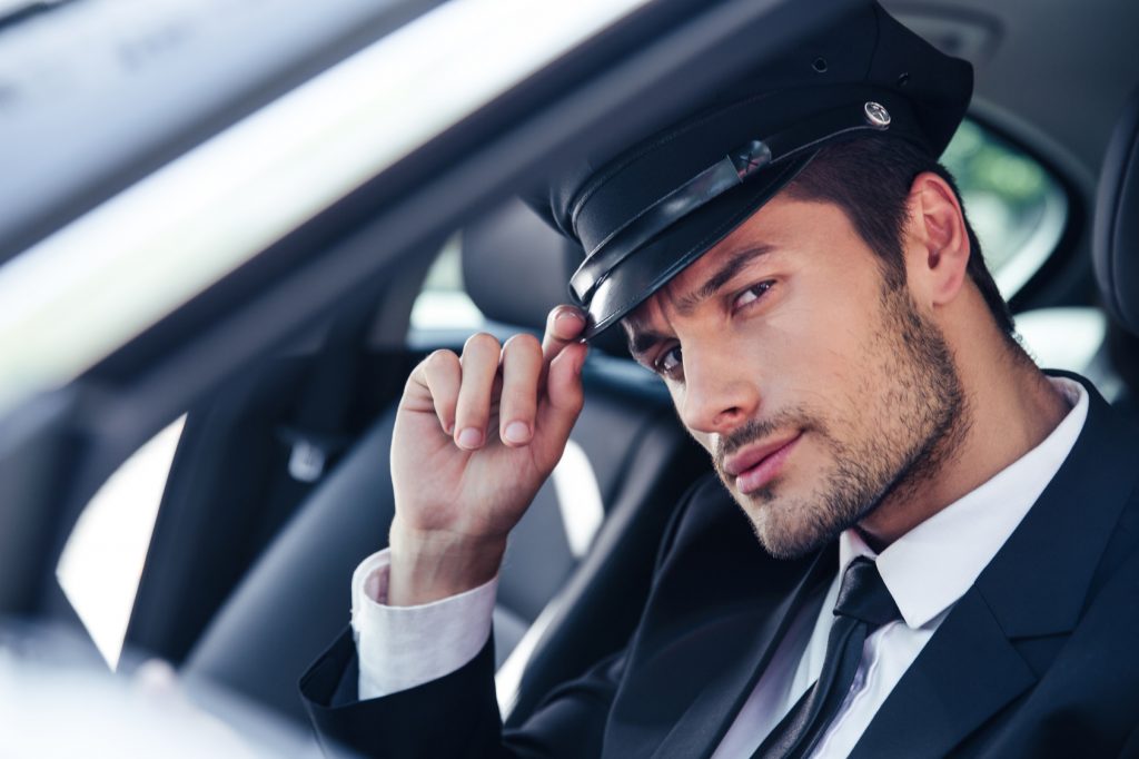 Portrait of a handsome male chauffeur sitting in a car and making saluting gesture